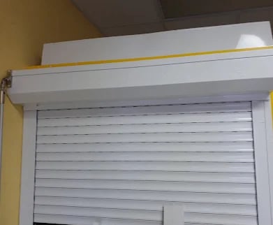 White roll-up hurricane shutter mounted above a window in its housing