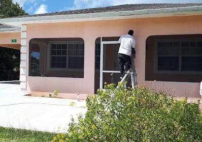Installer fitting an aluminum frame to a window opening from a ladder